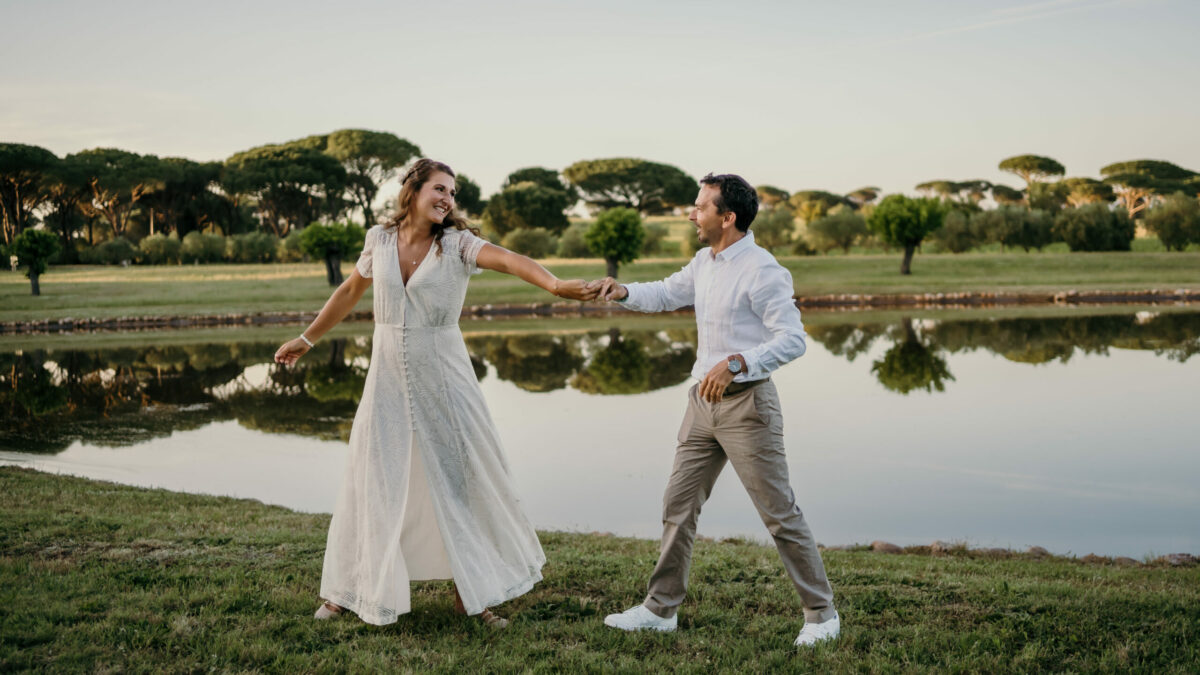 Les mariés se tiennent la main et dansent au bord d'un lac, des pins parasols à l'horizon