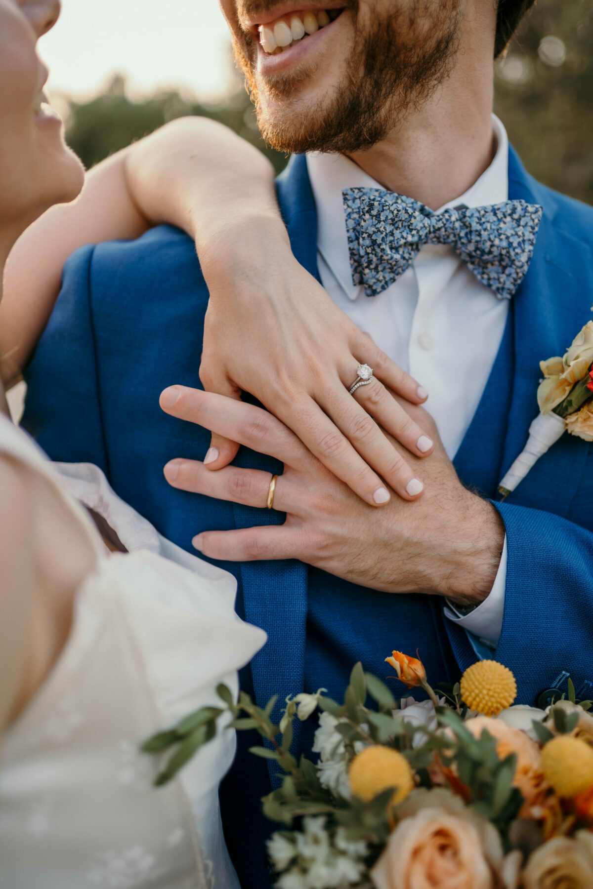 La mariée pose sa main sur la poitrine du marié en costume bleu et nœud papillon fleuri