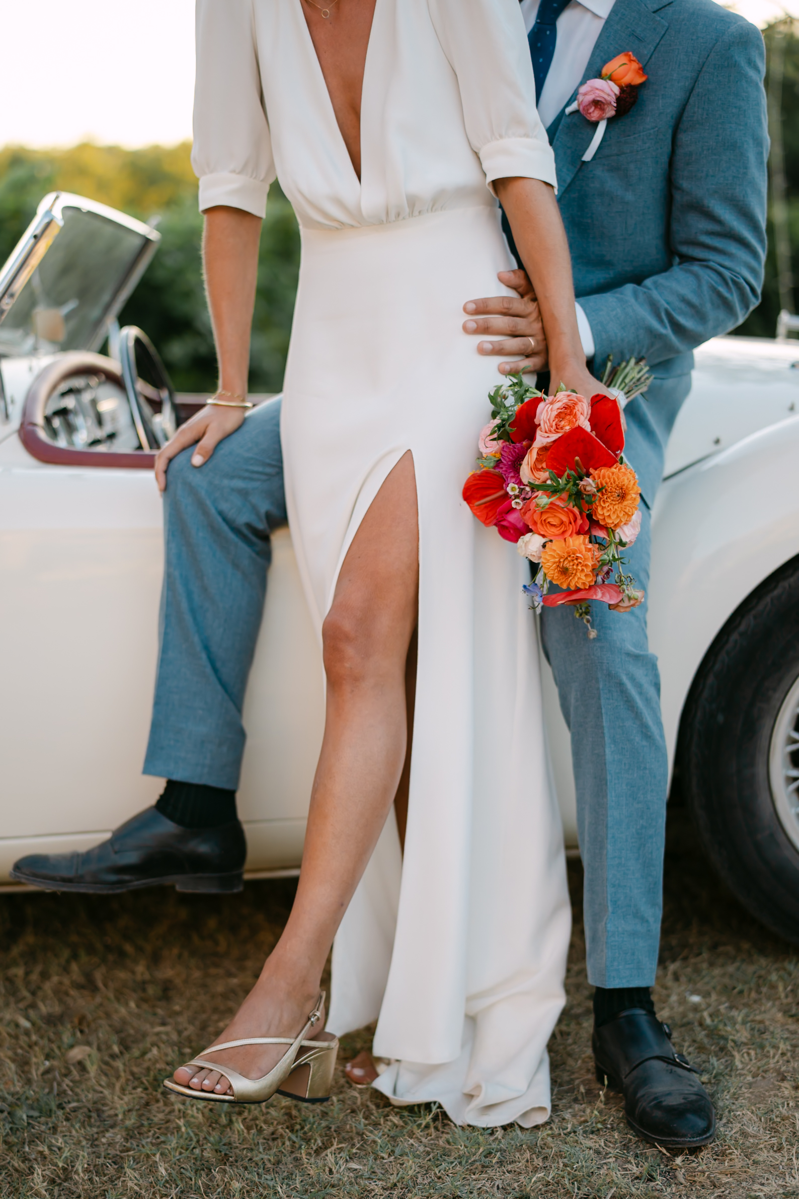 Photographe mariage Grimaud 7 La mariée appuyée contre une voiture ancienne, un bouquet orange contre le costume bleu du marié