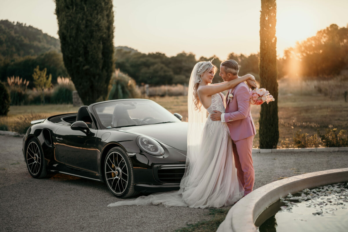 Les mariés s'enlacent près d'une Porsche noire décapotable, au coucher du soleil