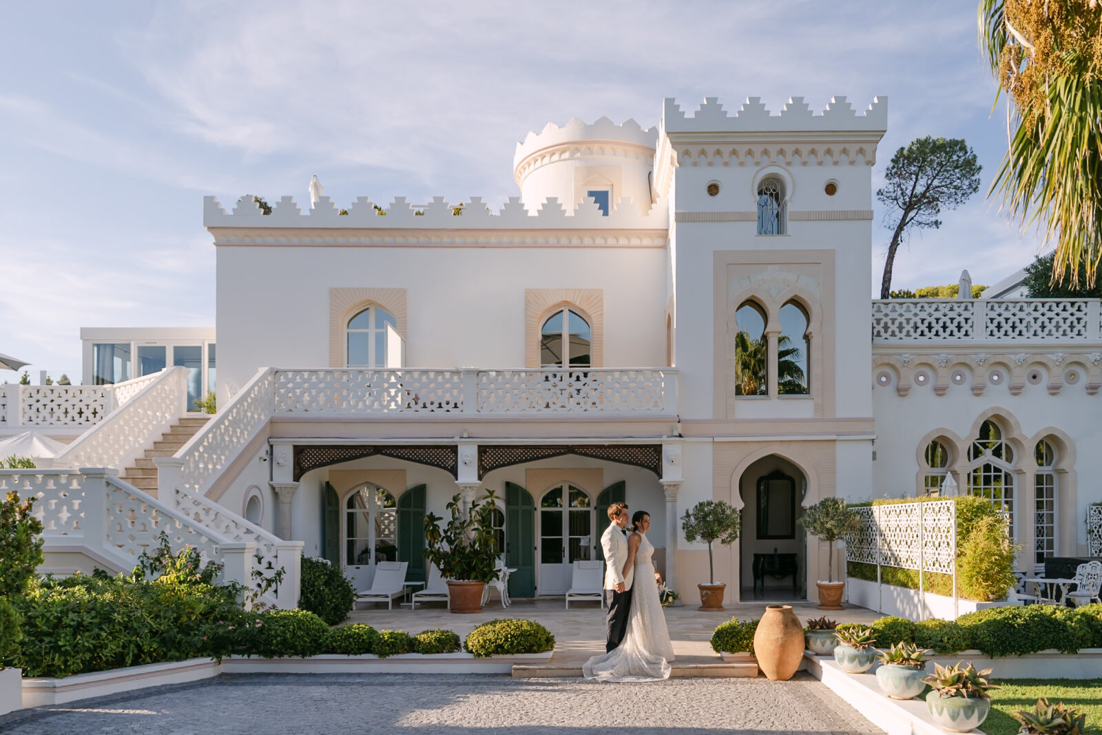 Photographe mariage château Provence 3 La façade d'un château blanc aux créneaux, les mariés au pied de l'escalier
