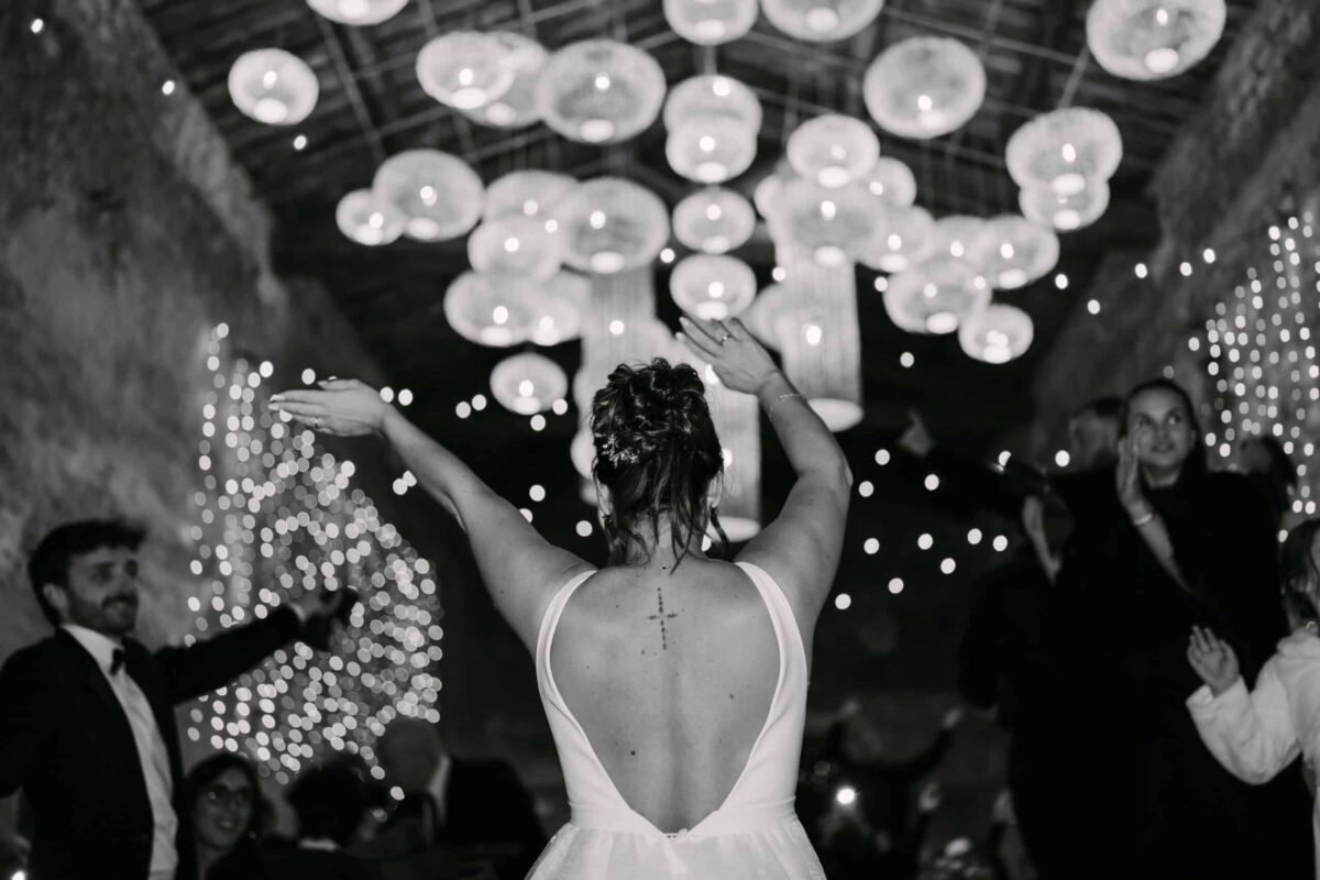 En noir et blanc, la mariée de dos danse sous des suspensions lumineuses
