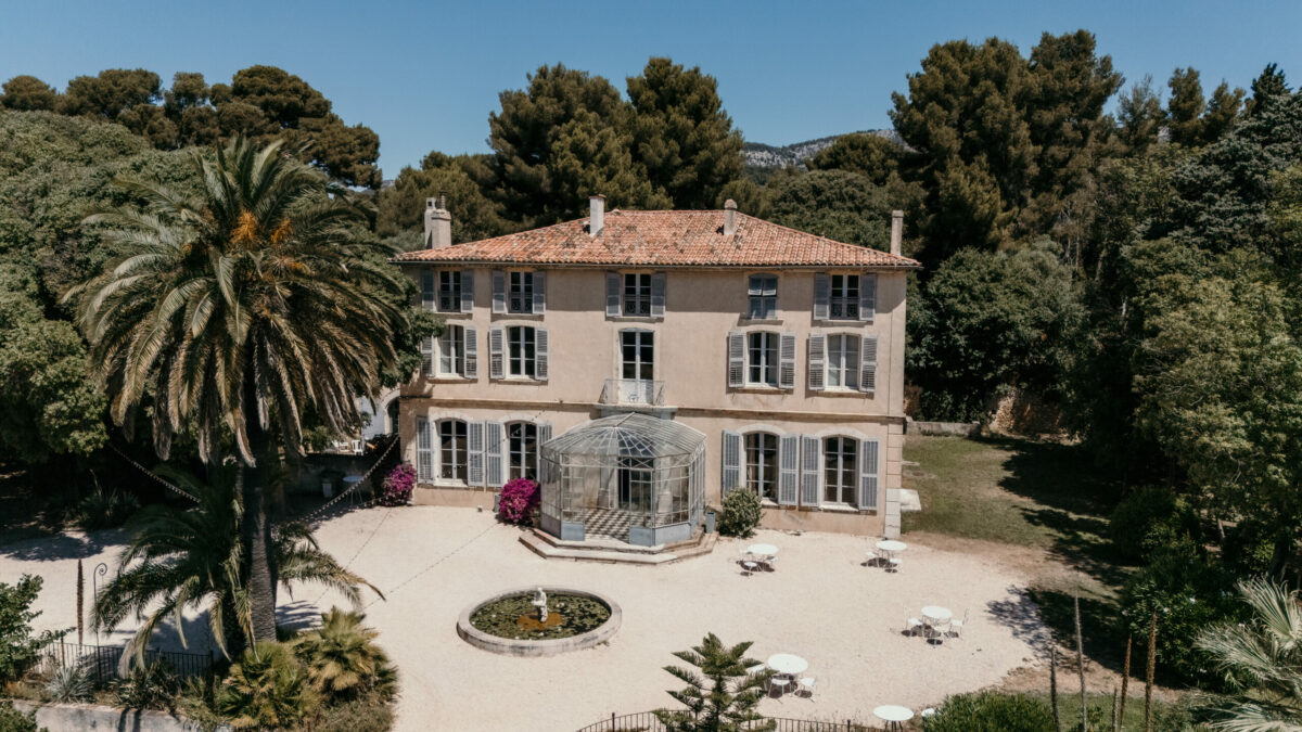 Vue aérienne d'une bastide rose et de sa cour, au milieu des pins
