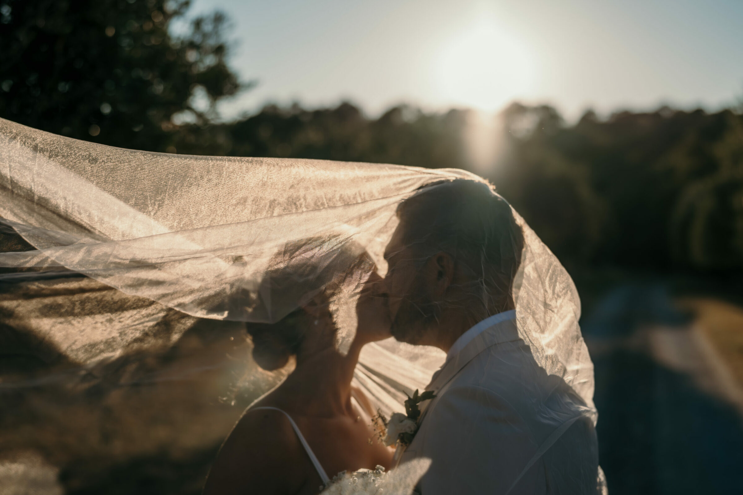 Sous le voile éclairé par le soleil couchant, les mariés s'embrassent