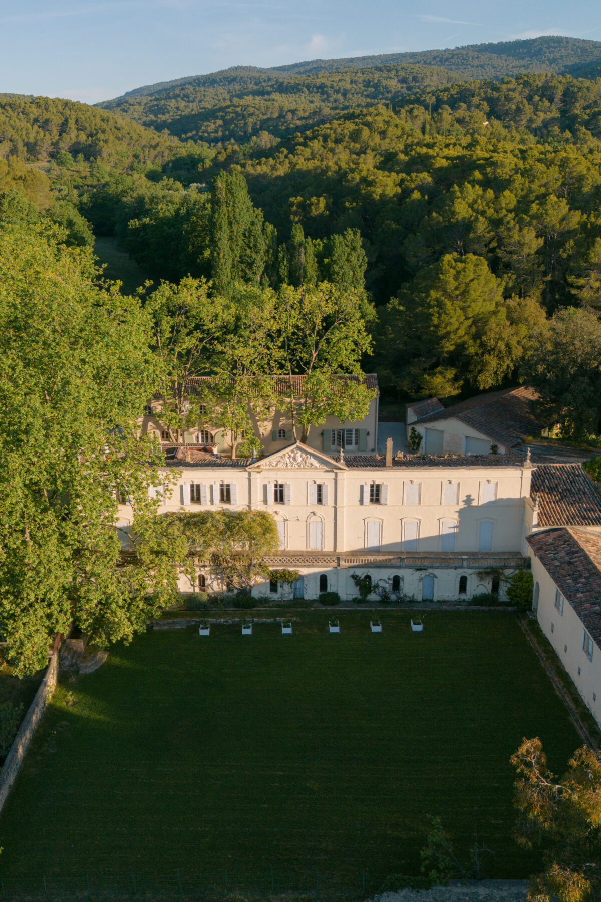 Accueil 96 Vue aérienne d'une bastide entourée de forêt et de collines, devant une grande pelouse