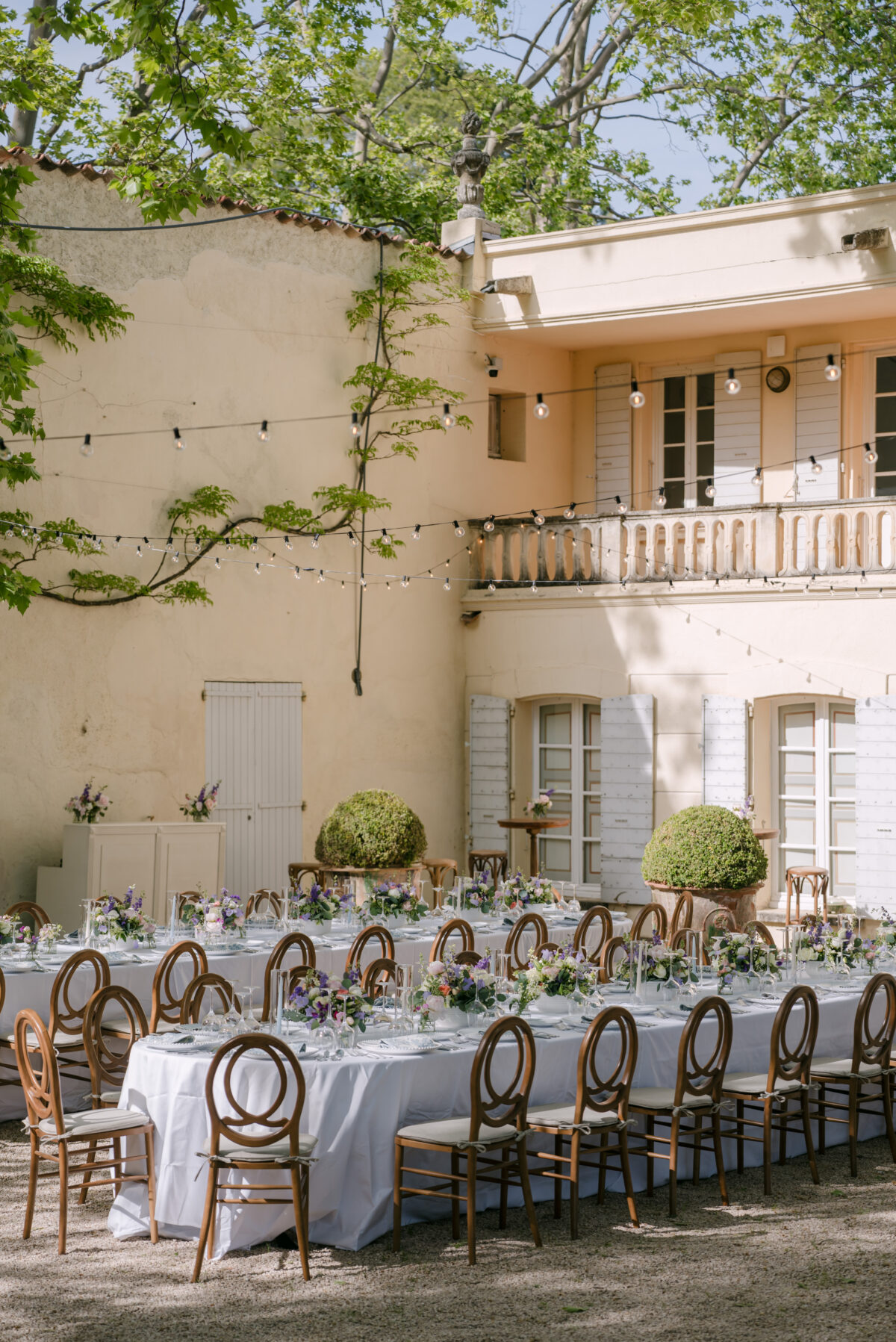 Accueil 3 Longues tables dressées devant la façade d'une bastide aux volets clairs, guirlandes lumineuses au-dessus