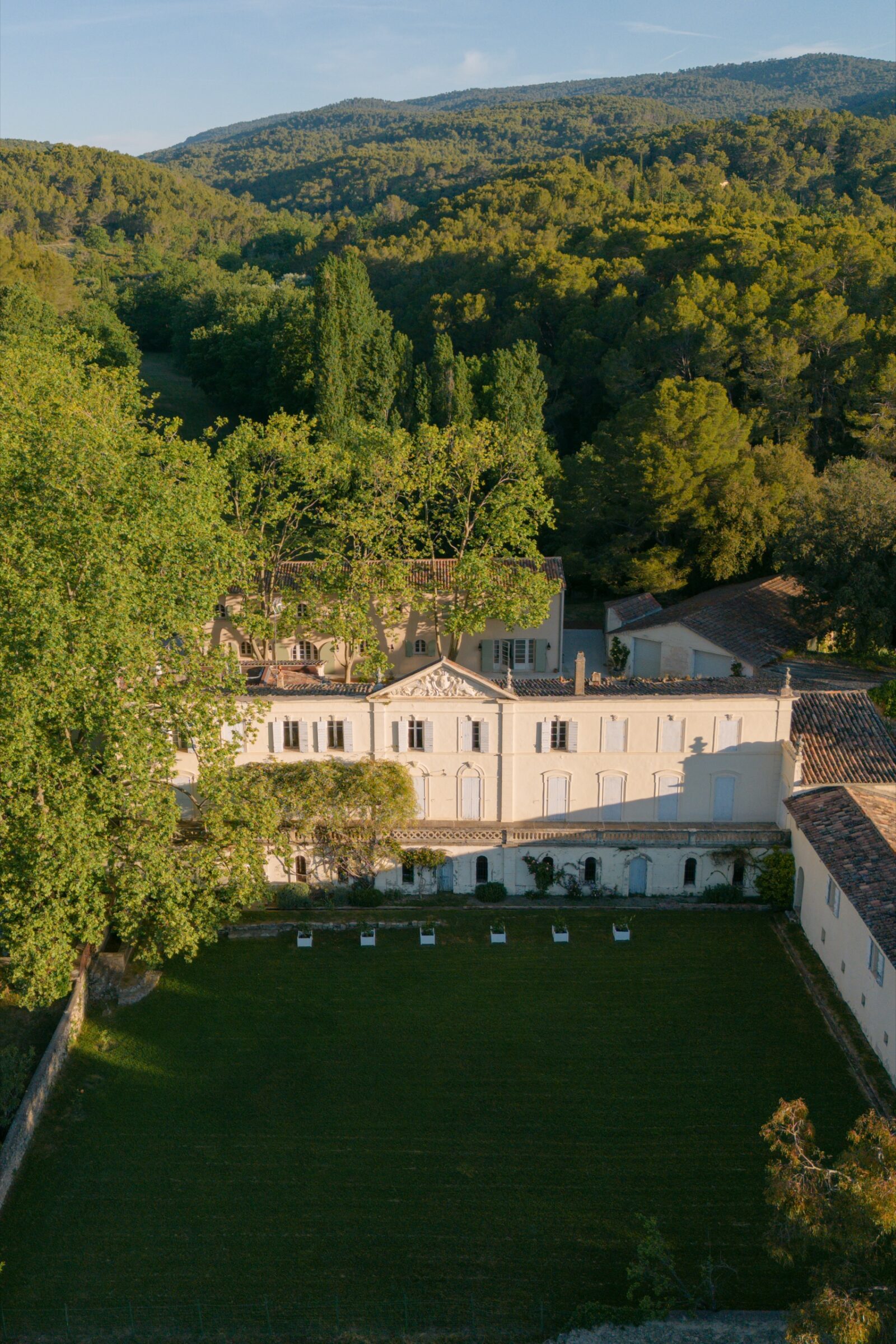 Photographe mariage Villecroze 5 Vue aérienne d'une bastide provençale au pied des collines boisées, devant une grande pelouse