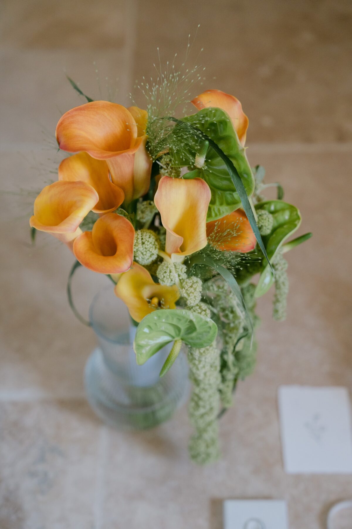 Bouquet de callas orange et de feuillages dans un vase, sur une table en pierre