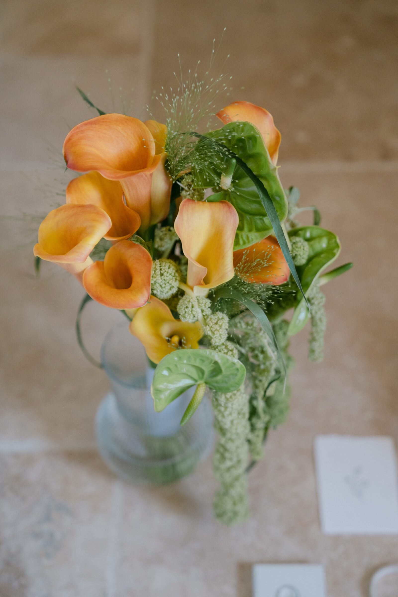 Photographe mariage haut de gamme Provence 9 Bouquet de callas orange et de feuillages dans un vase, sur une table en pierre