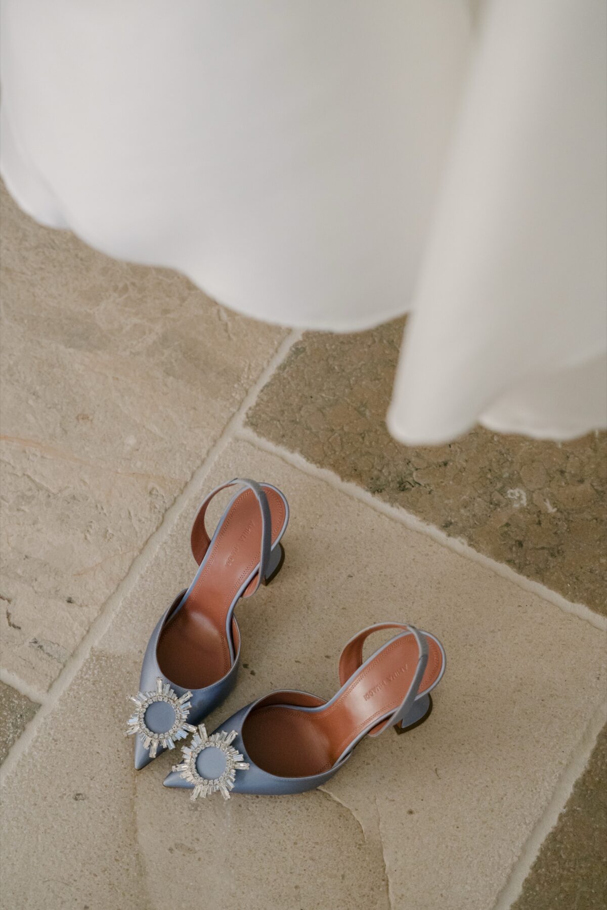 Les chaussures de la mariée posées sur une dalle de pierre, au pied de sa robe