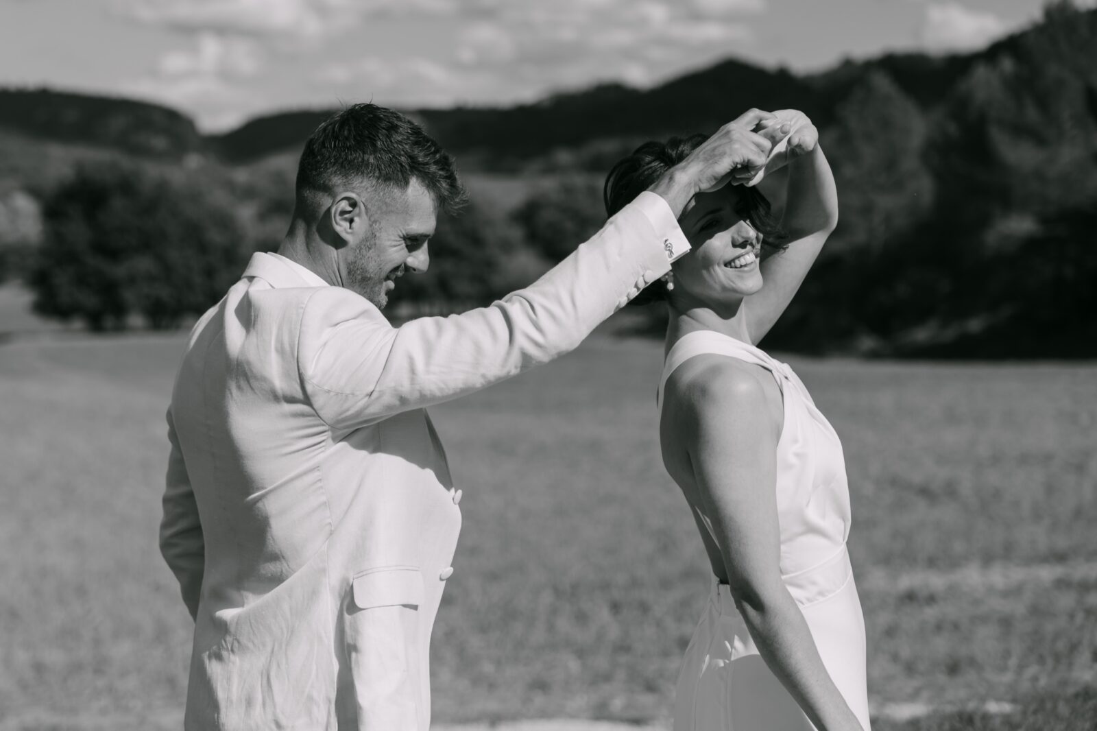 Accueil 13 En noir et blanc, le marié fait tourner la mariée au milieu d'un champ, les collines à l'horizon