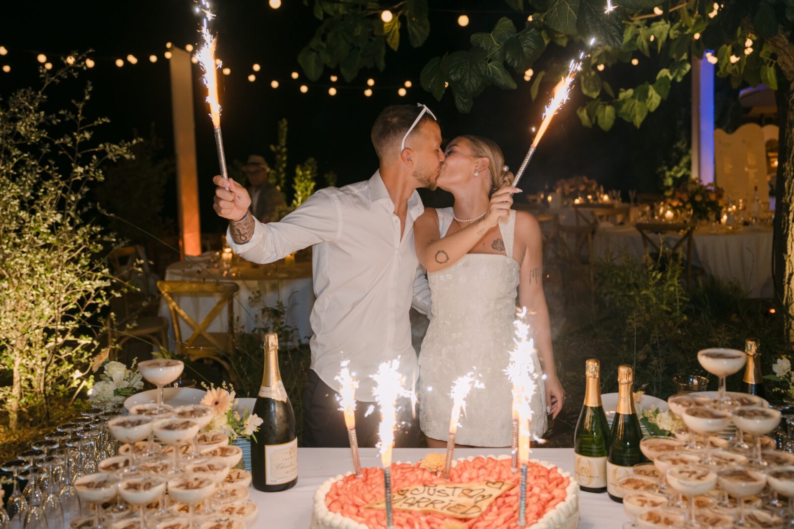 Un mariage en Provence en été : chaleur, lumière et photos 9 La nuit, les mariés s'embrassent derrière le gâteau, des fontaines d'étincelles allumées, sous les guirlandes