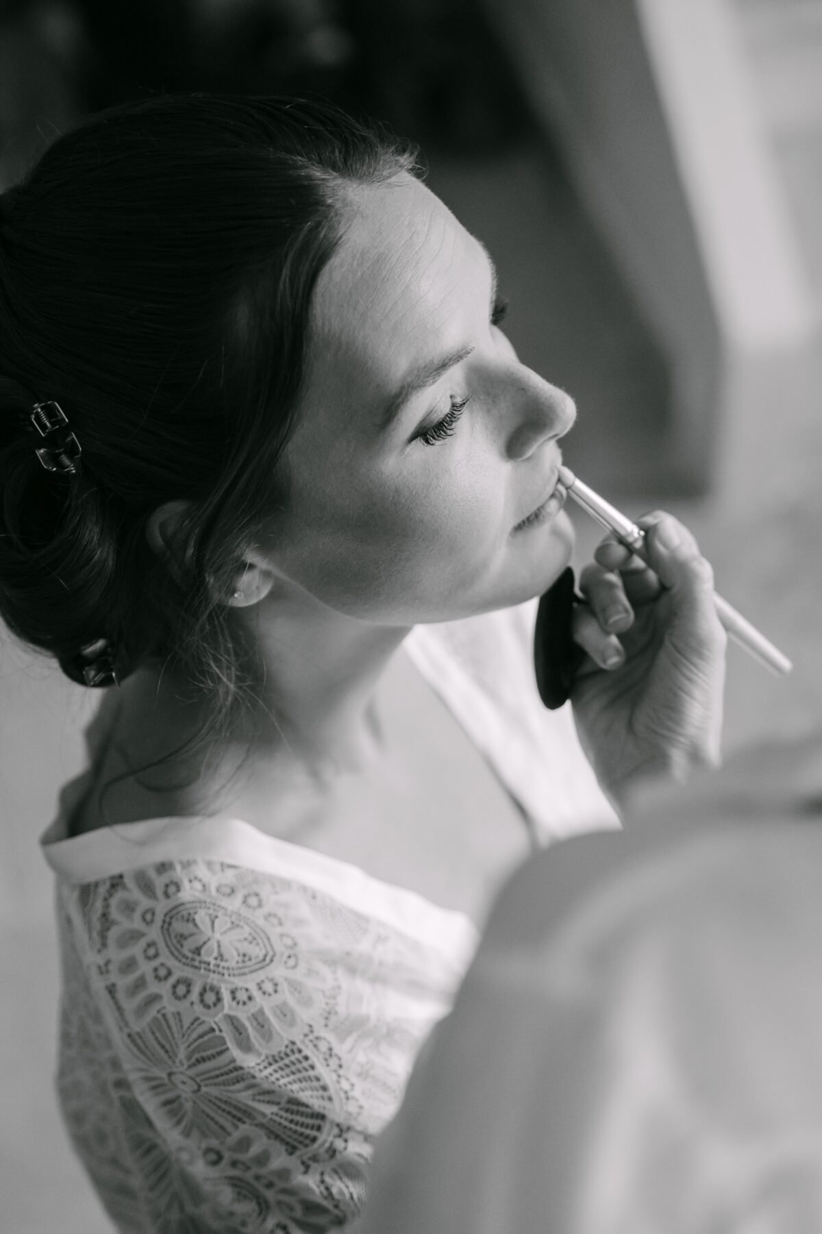 En noir et blanc, la mariée de profil pendant qu'on termine son maquillage