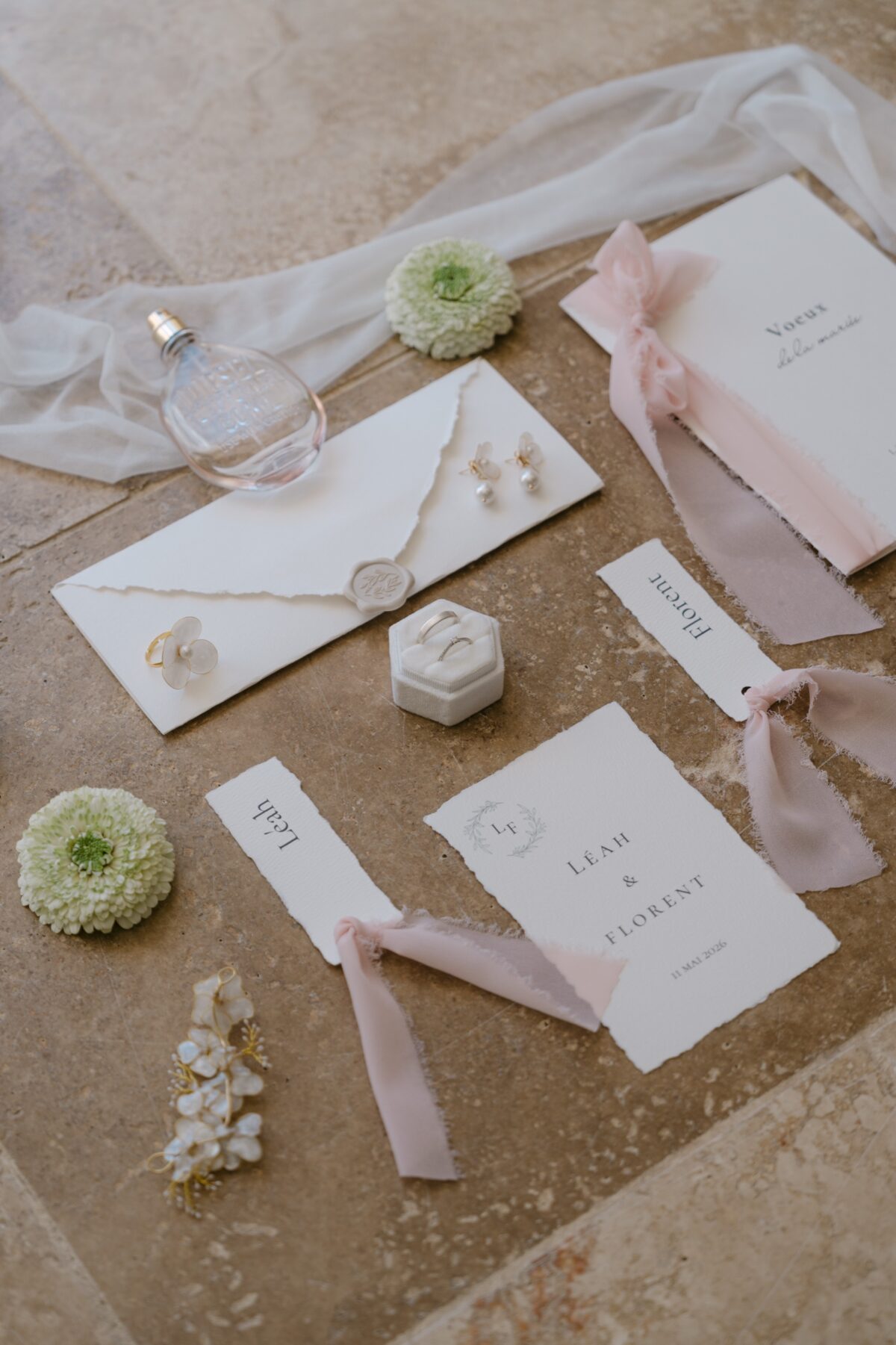 Faire-part, rubans rose poudré et fleurs blanches disposés sur une pierre claire