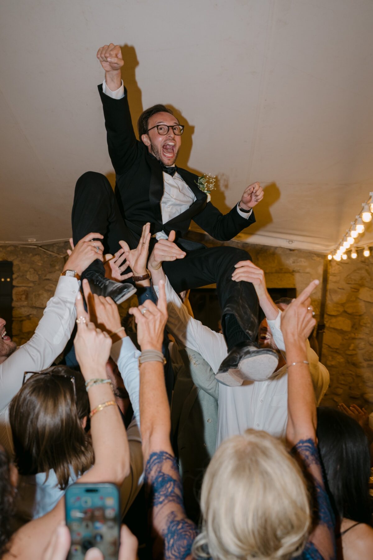 Les photos de vos invités de mariage : la moitié de l’histoire 4 Le marié, porté à bout de bras par ses amis, lève le poing en riant