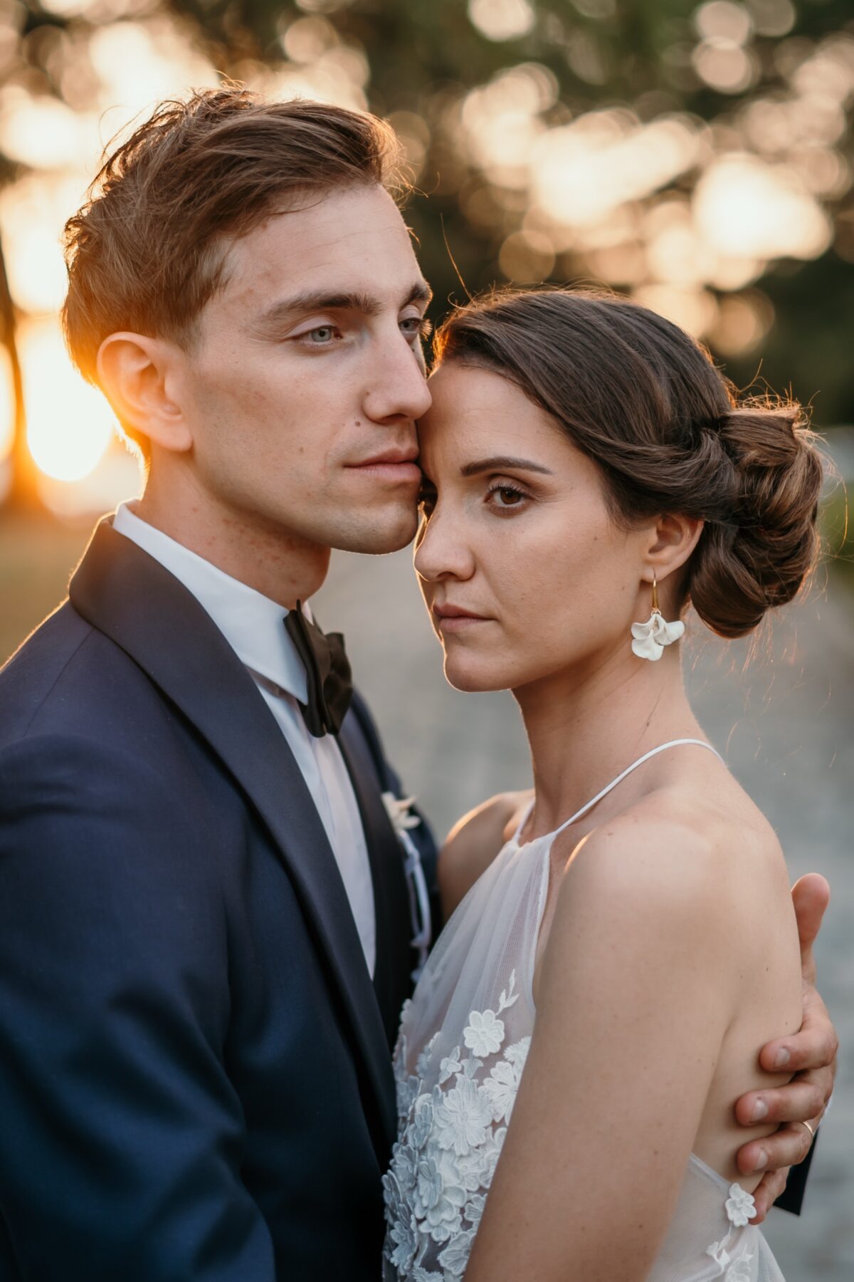 Portrait des mariés joue contre joue dans la lumière du soir, le marié en smoking bleu nuit