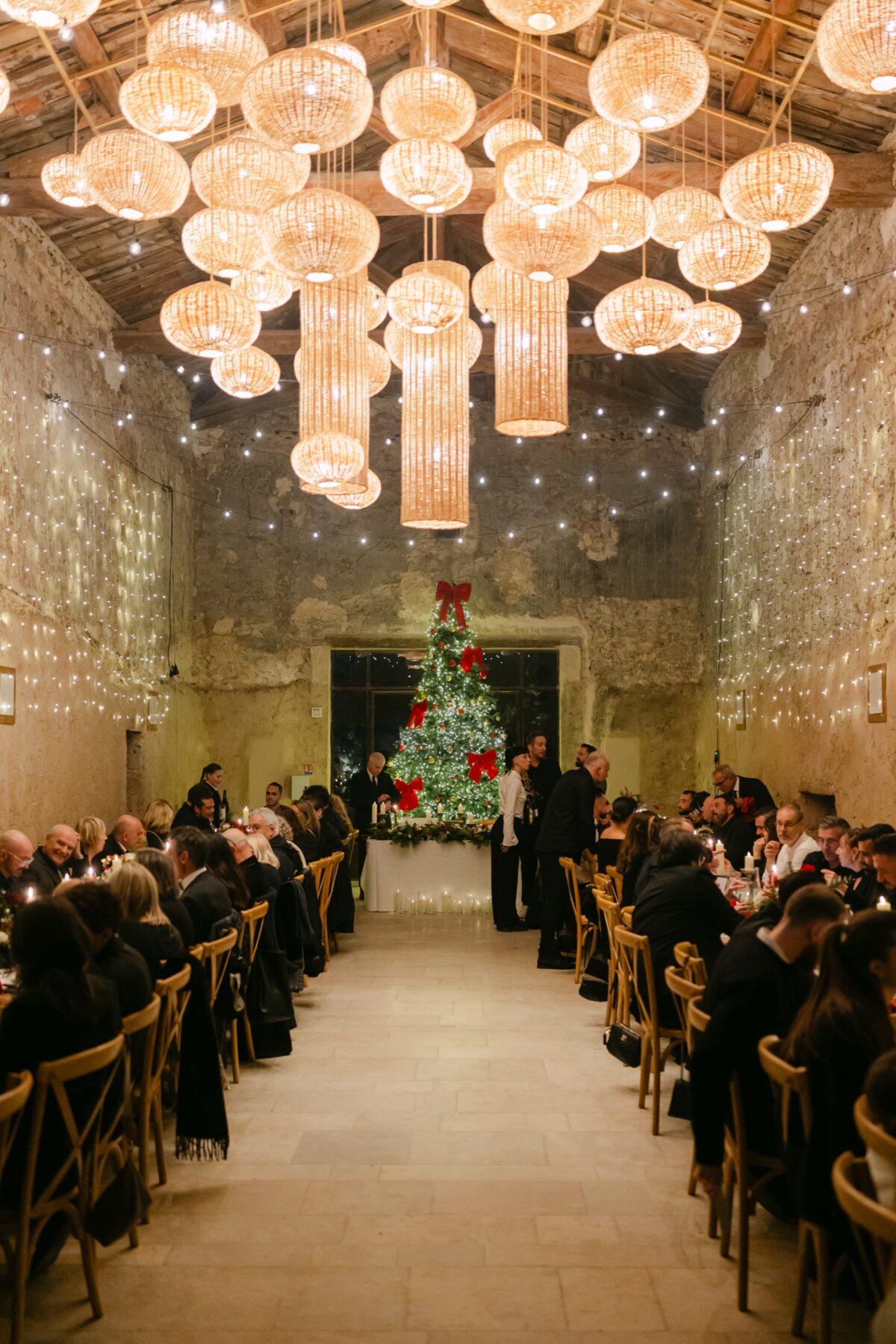 Mariage d'hiver : une salle voûtée en pierre éclairée par des dizaines de suspensions lumineuses, un sapin au fond