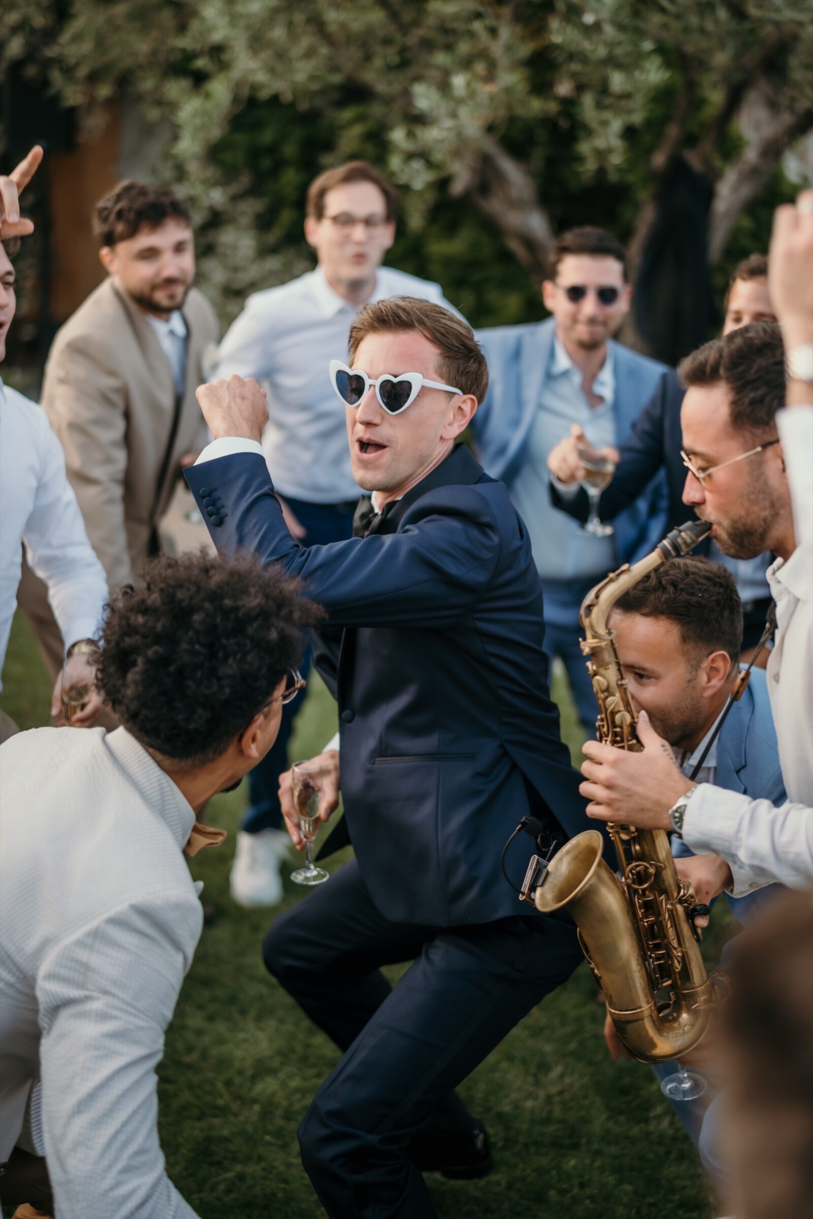 Mon approche 5 Un invité en lunettes de soleil danse au milieu des amis pendant qu'un saxophoniste joue