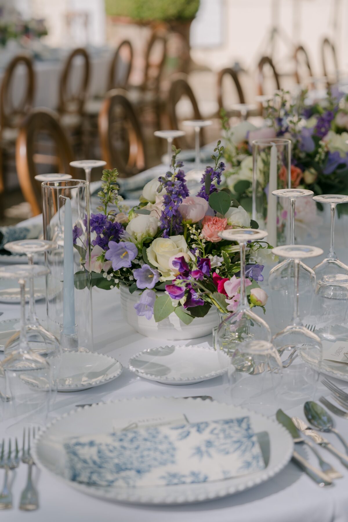 Table de mariage dressée avec de la vaisselle à motifs bleus et des bouquets de fleurs mauves
