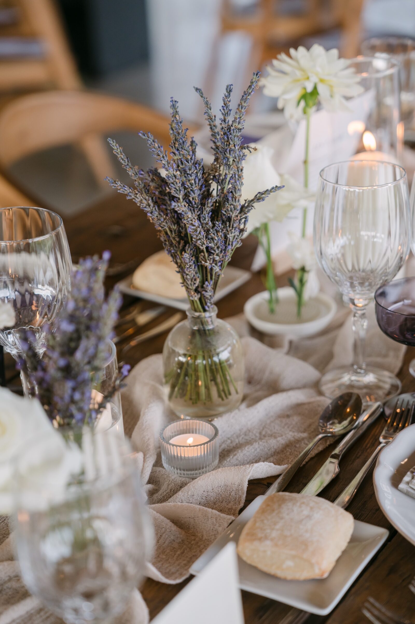 Photographe mariage Alpes-de-Haute-Provence 2 Sur une table en bois, un bouquet de lavande et de fleurs blanches entre les verres et les bougies