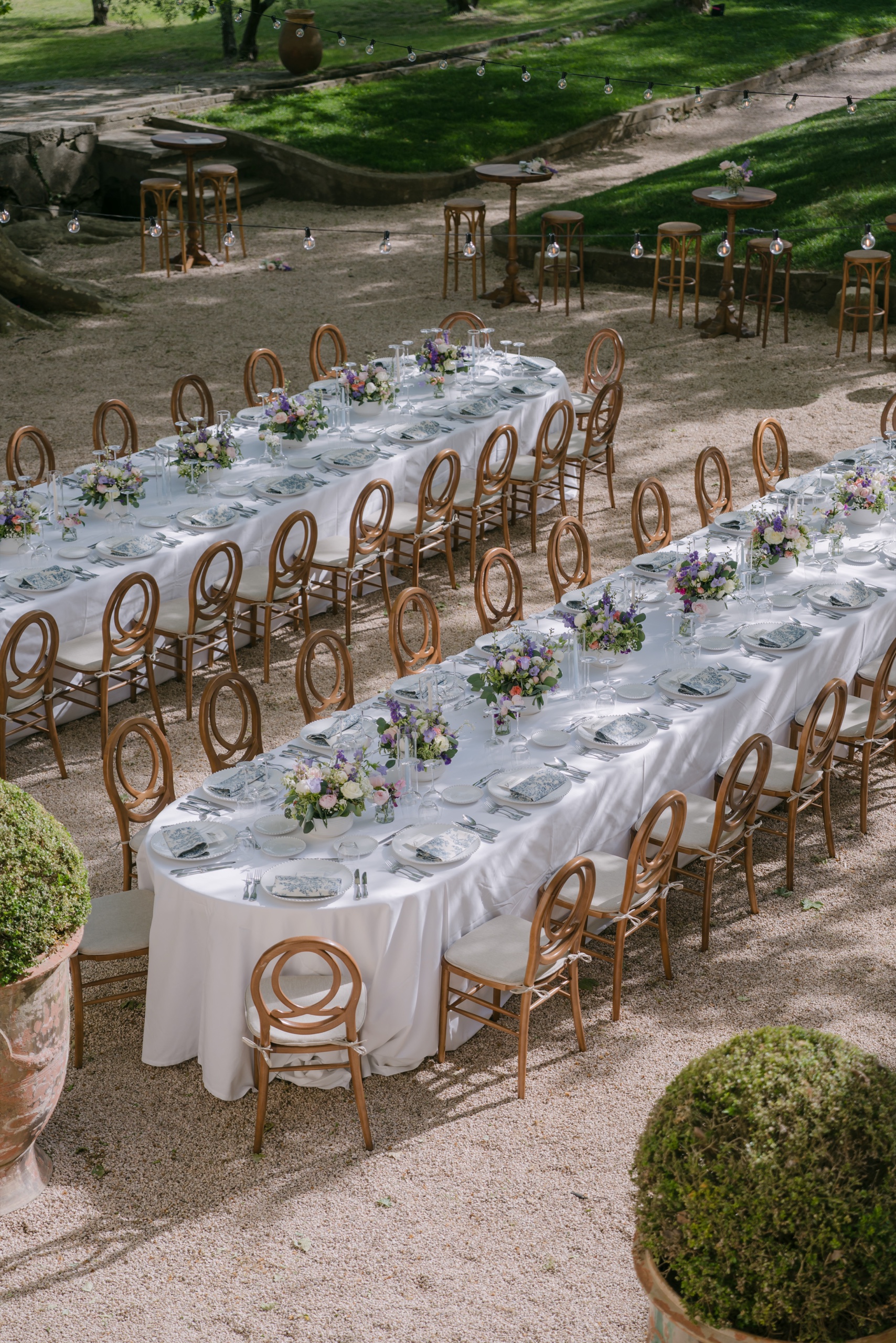 Un mariage en Provence en été : chaleur, lumière et photos 4 Longues tables blanches et chaises cannées sous les arbres de la cour d'une bastide, vues d'en haut