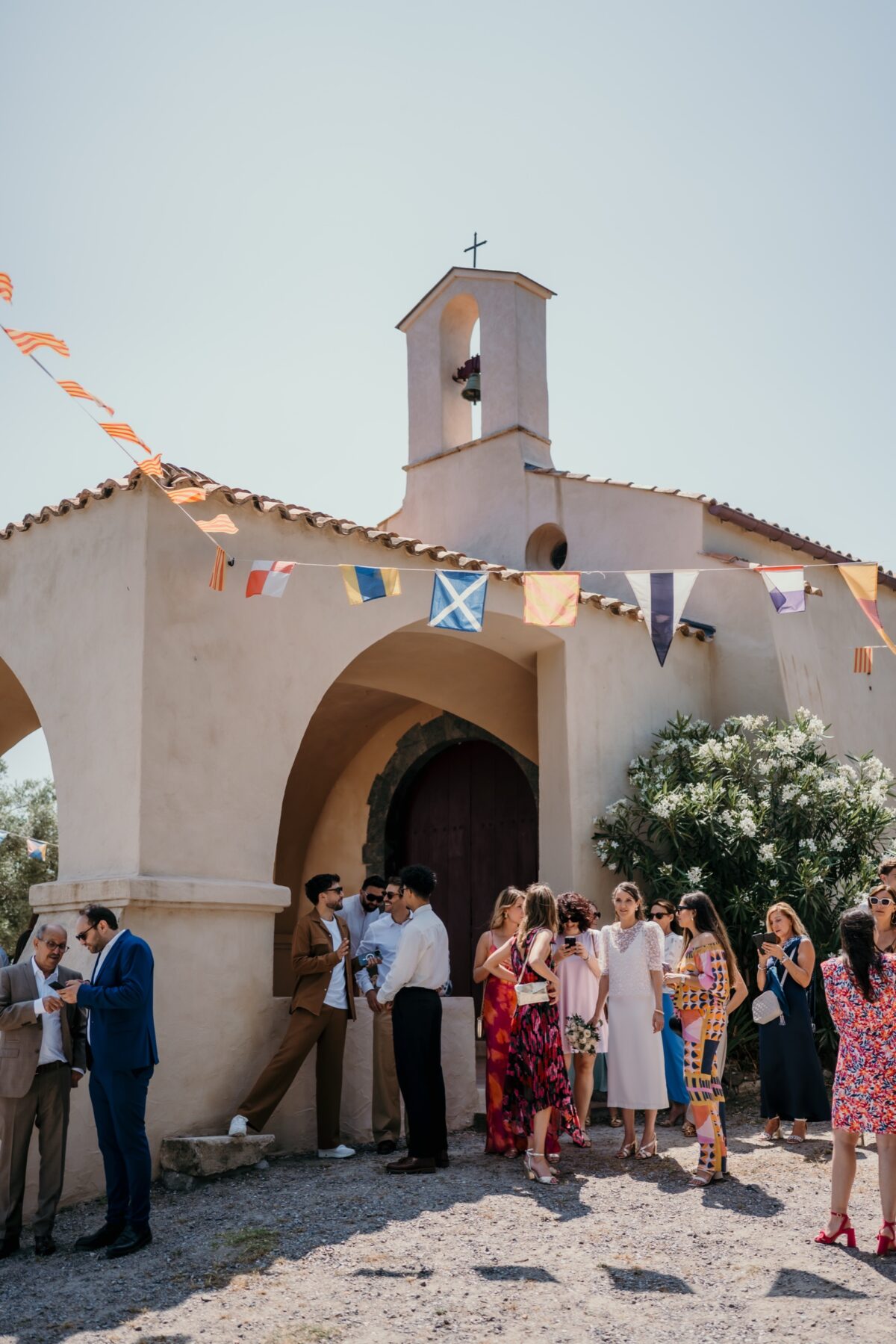 Les invités attendent devant une chapelle de village aux fanions colorés