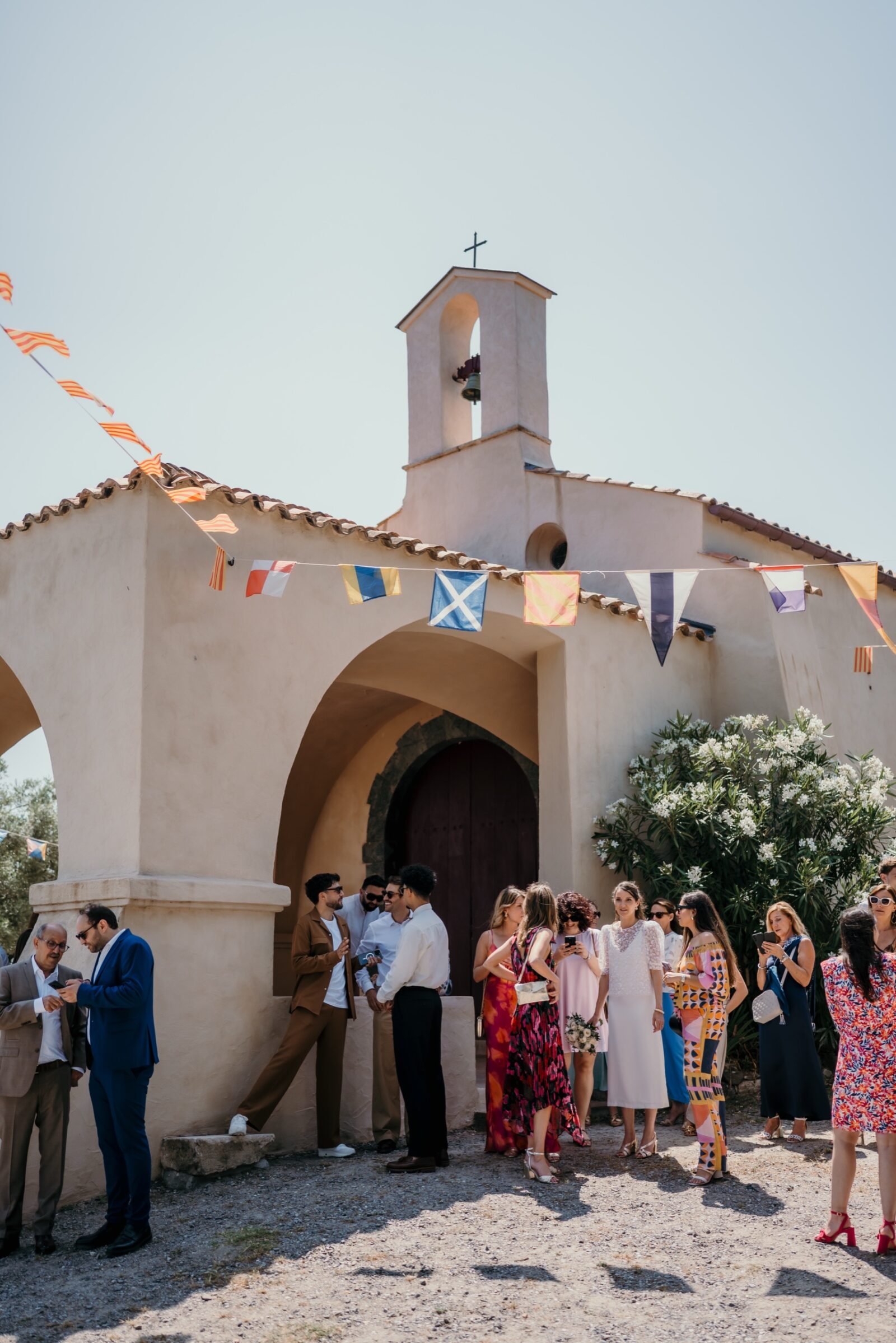 Photographe mariage Salernes 2 Les invités attendent devant une chapelle de village aux fanions colorés