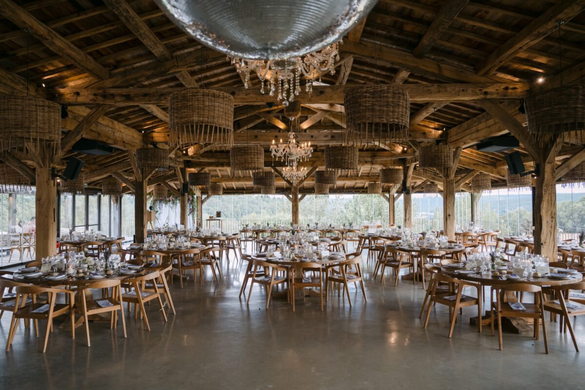 Grande halle en bois ouverte, tables rondes dressées sous une boule à facettes