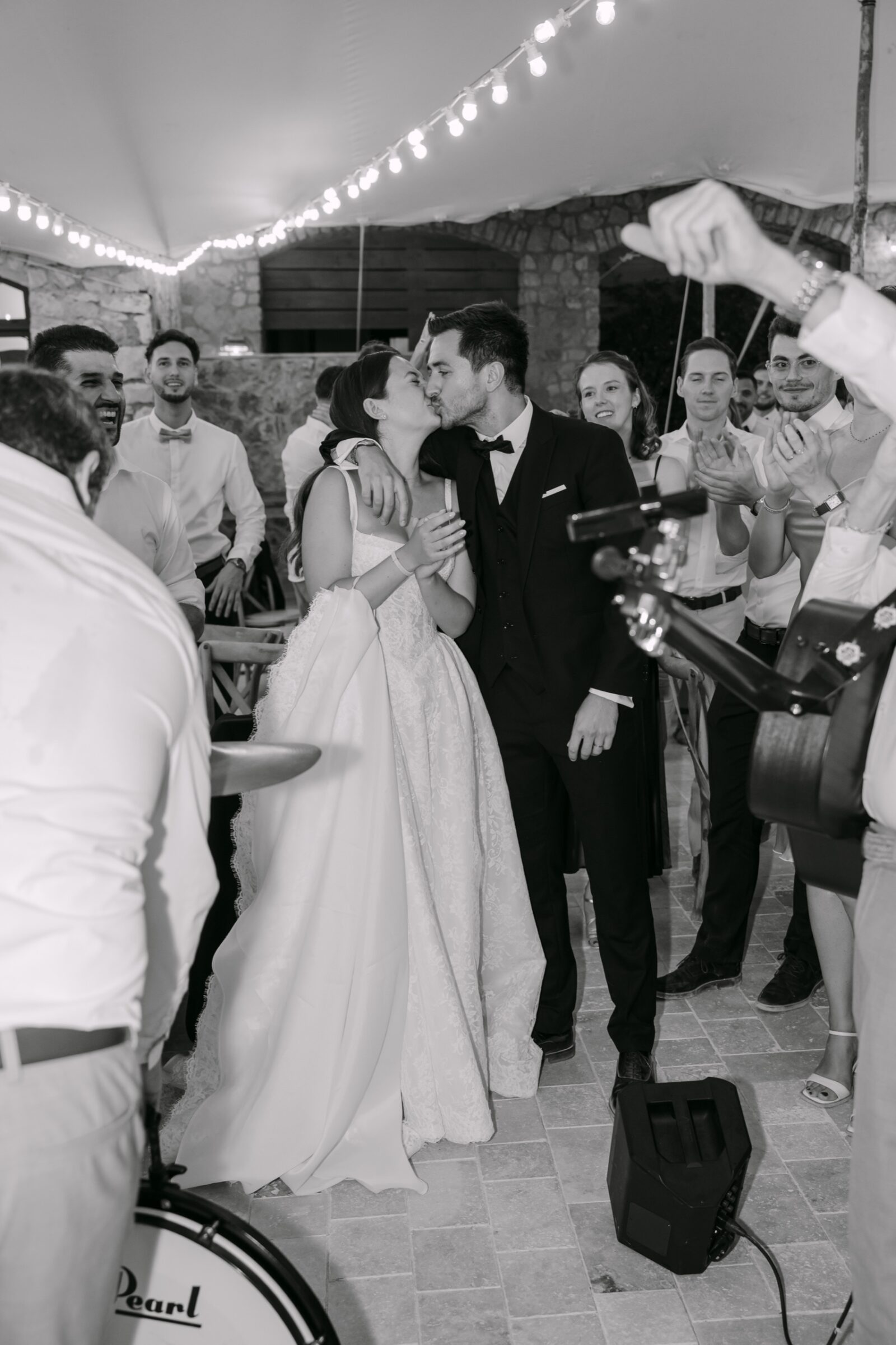 Après le mariage : tri, retouche et livraison de vos photos 7 En noir et blanc, les mariés s'embrassent sous les guirlandes pendant qu'un saxophoniste joue