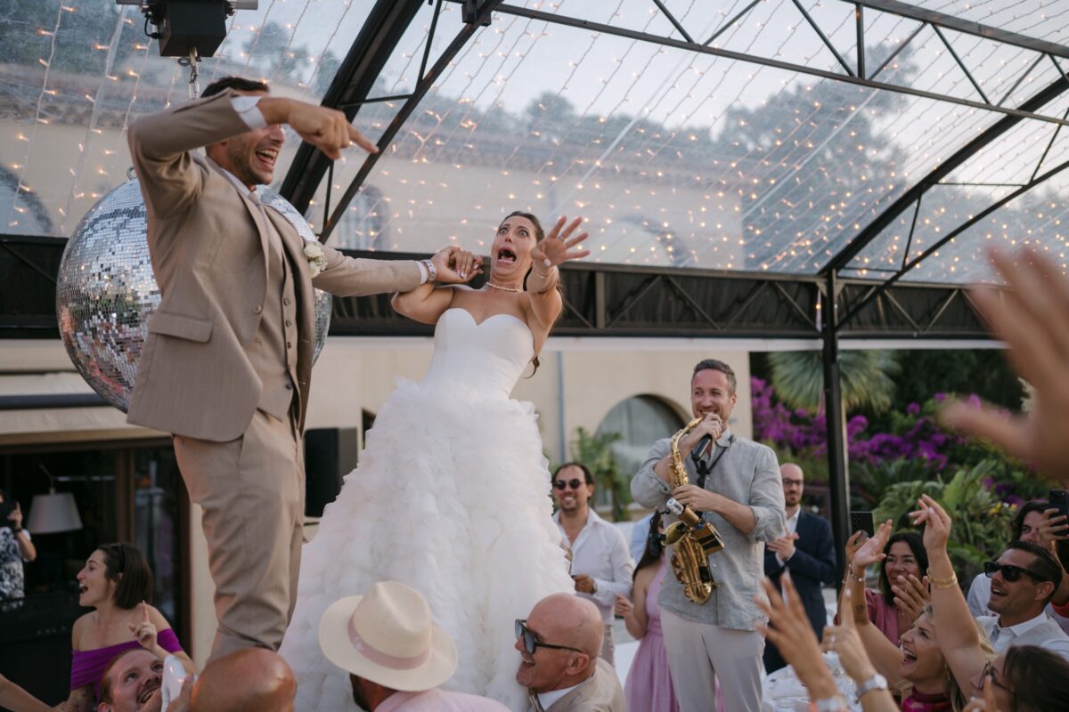 Sous une verrière, la mariée chante avec un saxophoniste au milieu des invités qui dansent