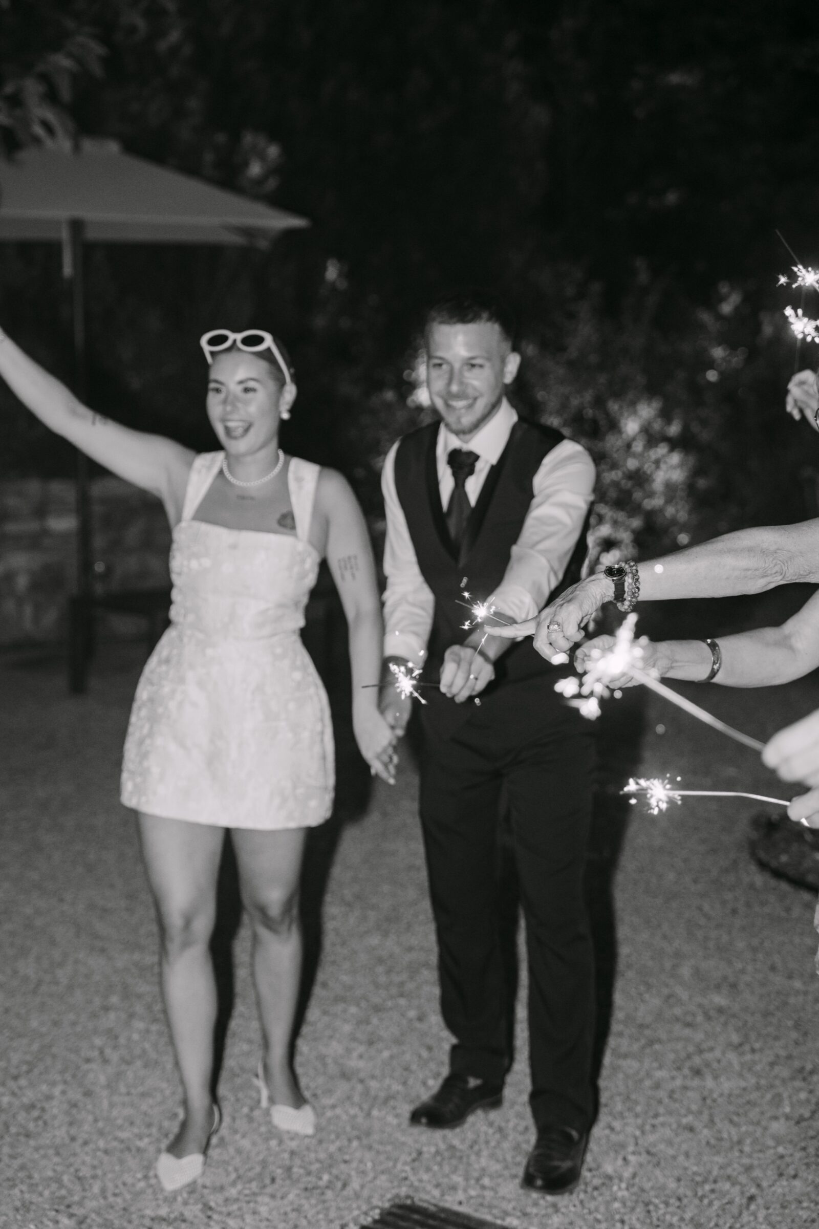 Photographe mariage Draguignan 10 En noir et blanc, les mariés sortent en riant entre les cierges magiques, la mariée en lunettes de soleil
