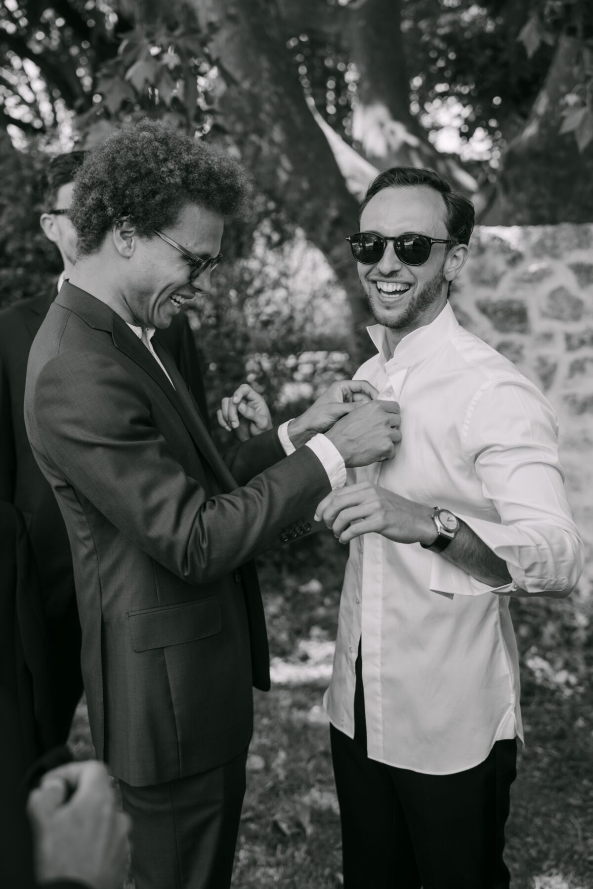En noir et blanc, deux amis du marié rient en ajustant leurs costumes